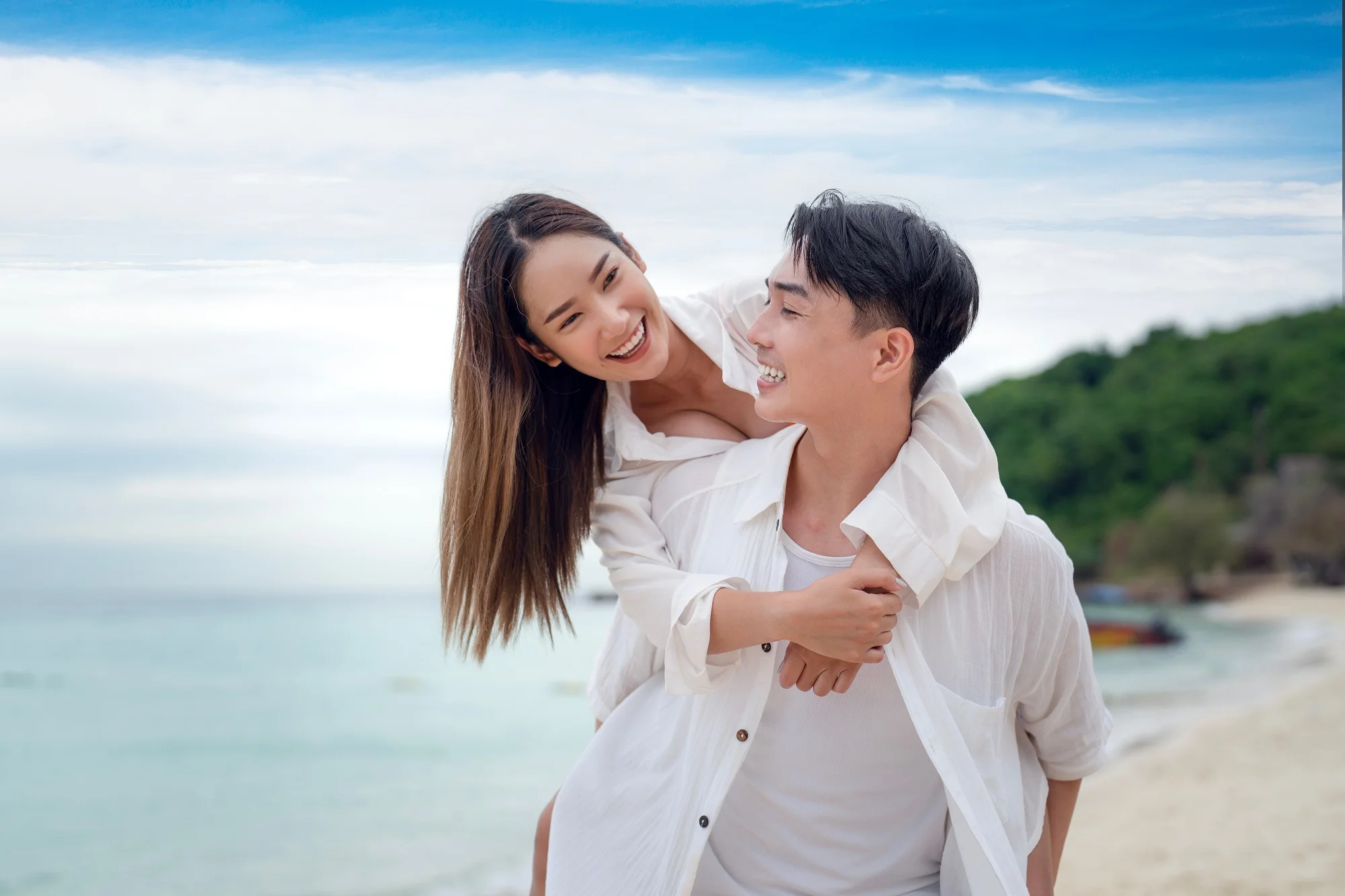 A happy couple enjoys a playful moment at the beach, with the woman on the man’s back as they both smile and look at each other - Dentist in Los Alamitos CA