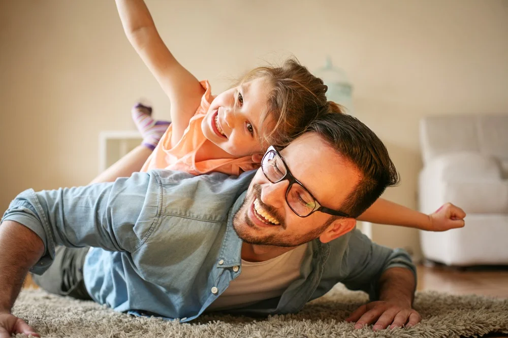 Father and daughter smiling and playing together on the floor - Dentist in Los Alamitos CA