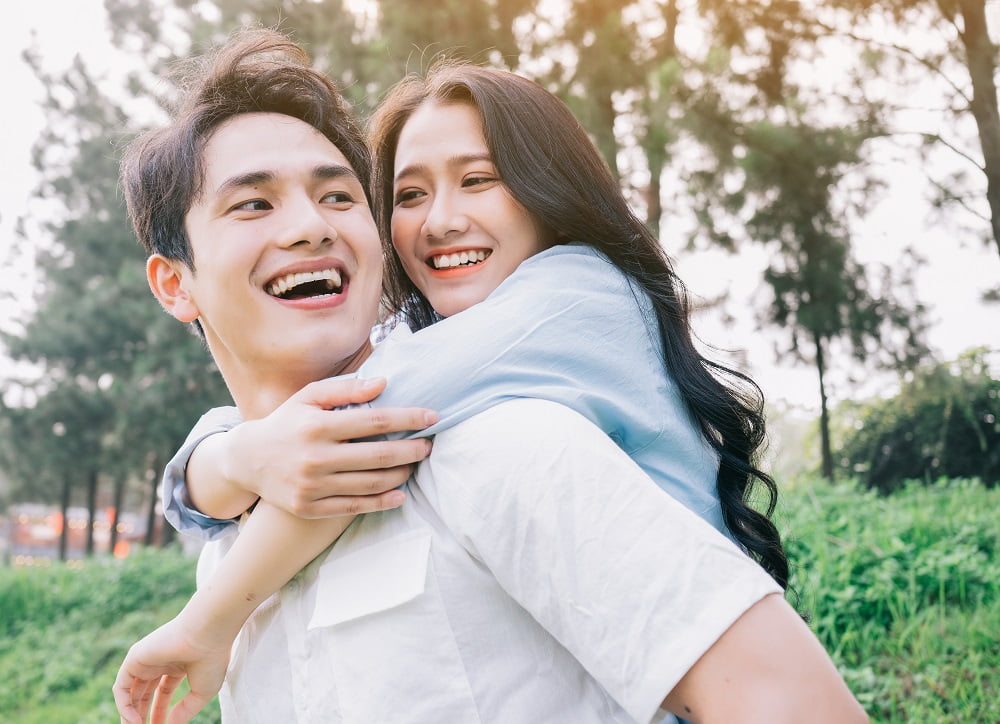 A happy couple enjoying a playful moment outdoors, with the woman giving the man a piggyback ride and both smiling brightly - smile makeover A happy couple enjoying a playful moment outdoors, with the woman giving the man a piggyback ride and both smiling brightly - smile makeover