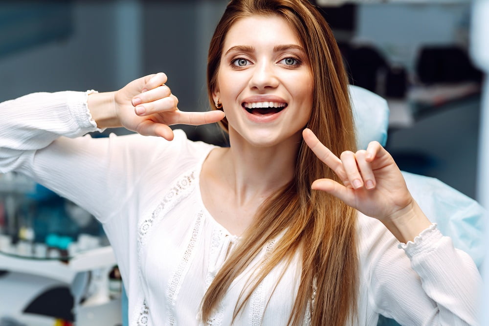 A smiling woman points to her teeth, showcasing a bright, healthy smile - veneers and dental laminates A smiling woman points to her teeth, showcasing a bright, healthy smile - veneers and dental laminates