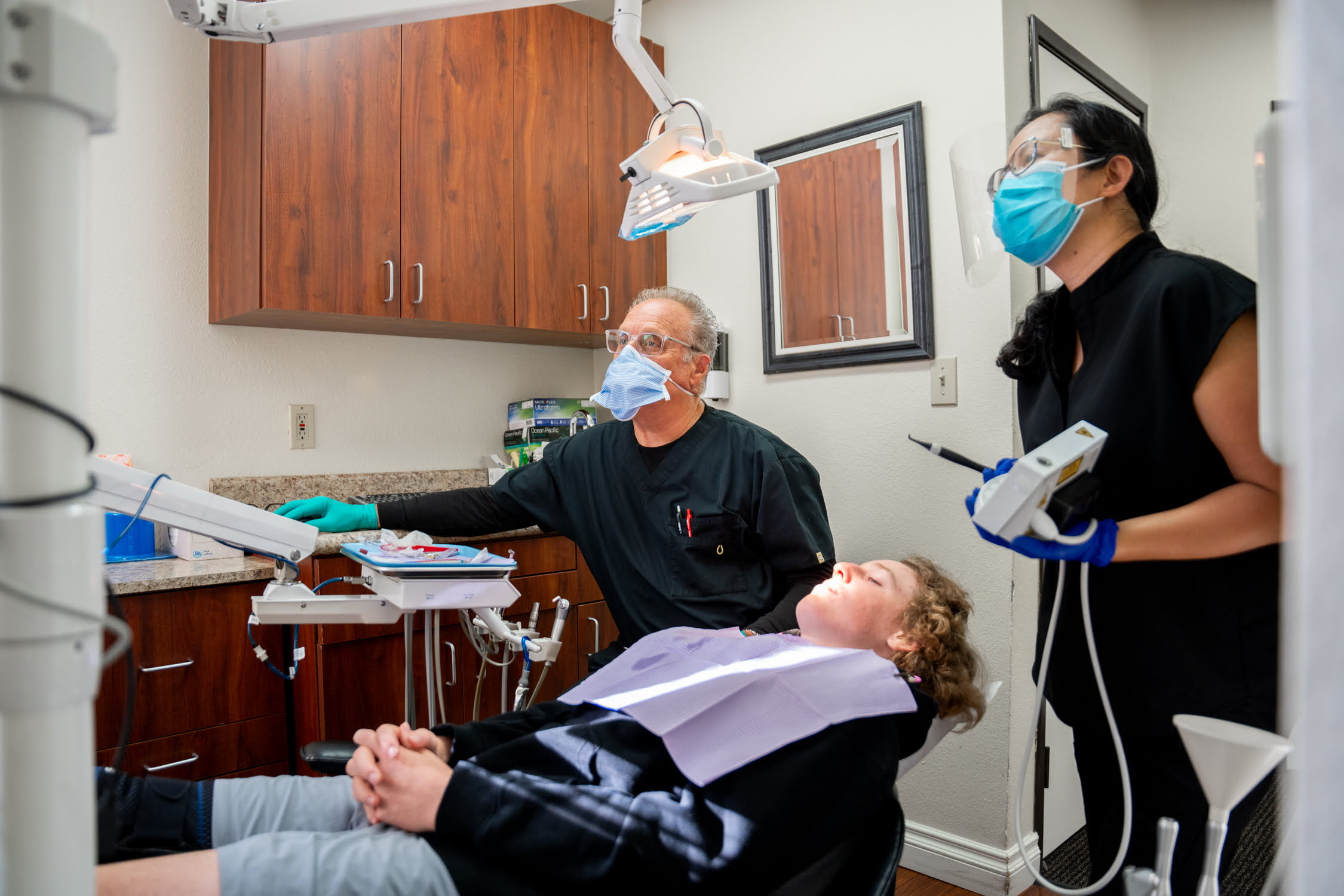 Dentist Dr. Chris Gipe and Dental Hygienist Quynh Duong prepare to examine a patient reclining in the dental chair - dentures Dentist Dr. Chris Gipe and Dental Hygienist Quynh Duong prepare to examine a patient reclining in the dental chair - dentures