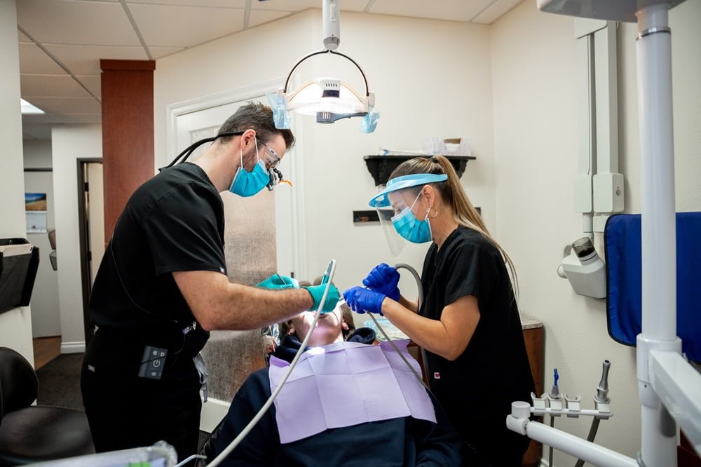 Two dental professionals in protective gear perform a procedure on a patient in a dental clinic - root canal Two dental professionals in protective gear perform a procedure on a patient in a dental clinic - root canal