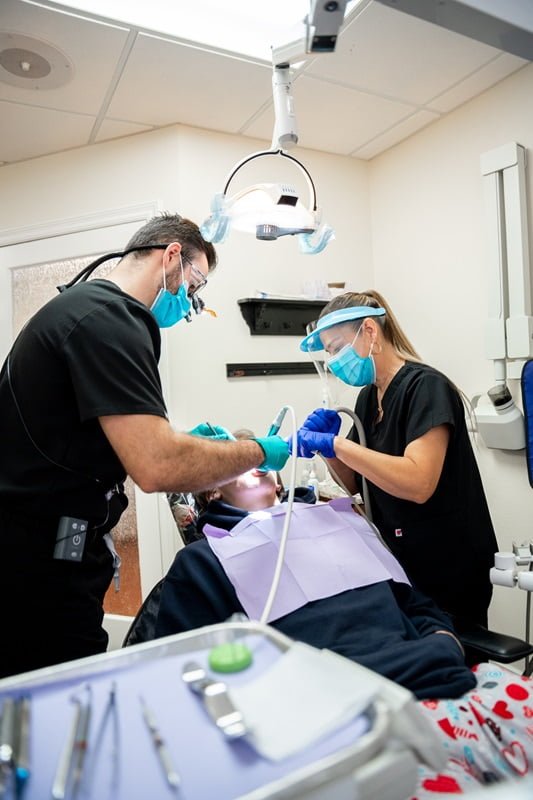 Two dental professionals in protective gear perform a procedure on a patient in a dental clinic - veneers and dental laminates Two dental professionals in protective gear perform a procedure on a patient in a dental clinic - veneers and dental laminates