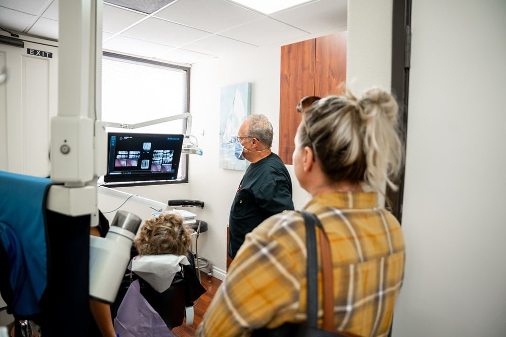 Dr. Chris Gipe reviews a patient’s dental X-rays on a monitor, while another person observes in the background - dental checkup Dr. Chris Gipe reviews a patient’s dental X-rays on a monitor, while another person observes in the background - dental checkup