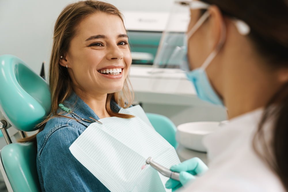 A woman smiles at her dentist during a dental check-up, sitting in a dental chair while the dentist prepares tools for the procedure - orthodontics A woman smiles at her dentist during a dental check-up, sitting in a dental chair while the dentist prepares tools for the procedure - orthodontics