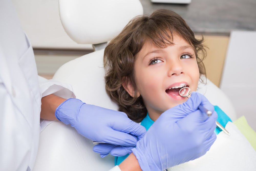 A child sits in a dental chair, receiving a checkup from a dentist wearing blue gloves - orthodontics A child sits in a dental chair, receiving a checkup from a dentist wearing blue gloves - orthodontics