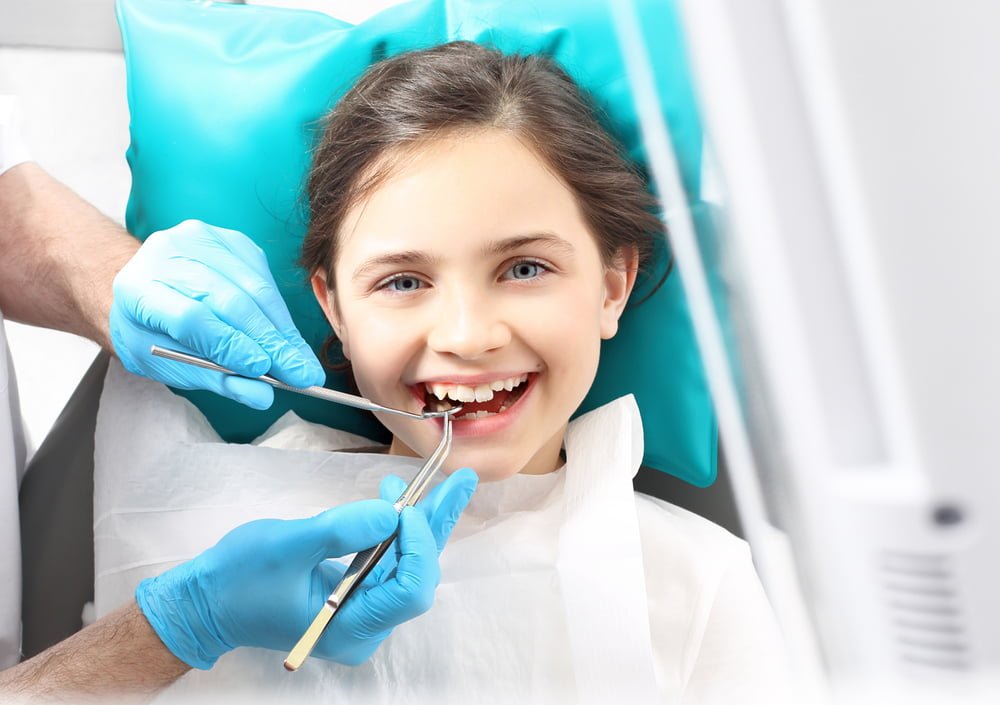 A young girl smiles during a dental check-up as the dentist examines her teeth with tools - root canal A young girl smiles during a dental check-up as the dentist examines her teeth with tools - root canal