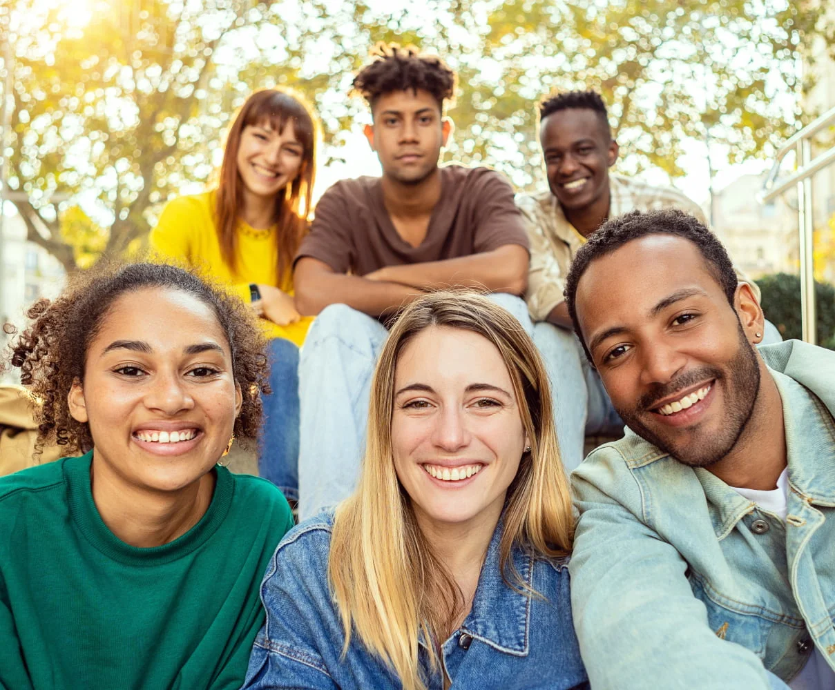 A group of six friends smiles at the camera while sitting outdoors on a sunny day, enjoying their time together - Dentist in Los Alamitos CA