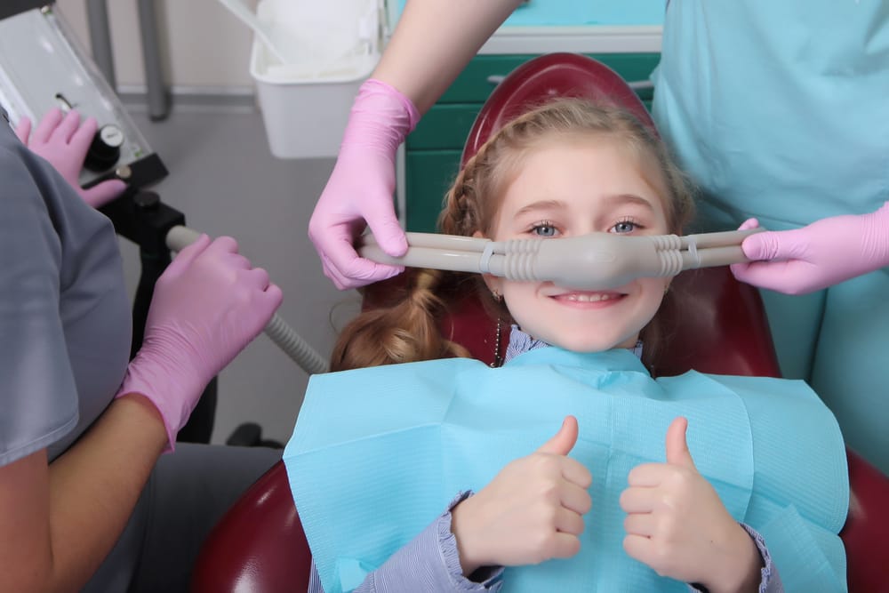 Child Receiving Nitrous Oxide Sedation – Sedation Dentistry in Long Beach CA A young girl gives a thumbs-up while receiving nitrous oxide at the dental office, showing how sedation dentistry helps children feel relaxed and comfortable – Sedation Dentistry in Long Beach CA.