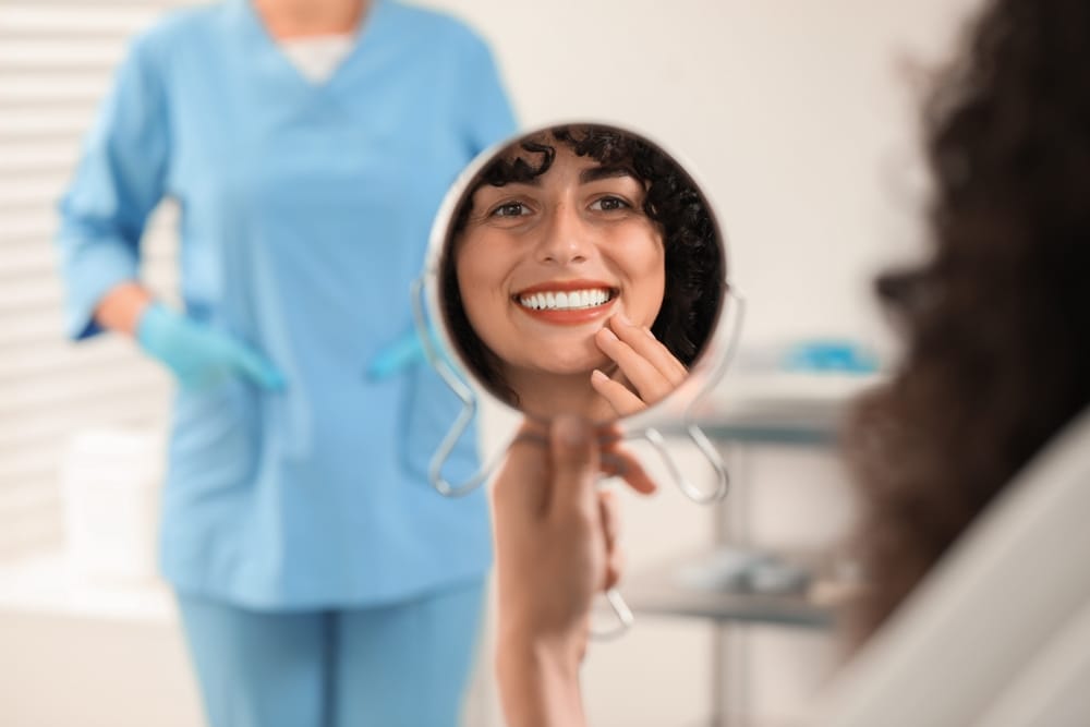 Smiling Woman Admiring Her Teeth After Sedation Treatment – Sedation Dentistry in Long Beach CA A woman smiles confidently into a mirror after her dental procedure, reflecting the calm and positive results of sedation-assisted care – Sedation Dentistry in Long Beach CA.