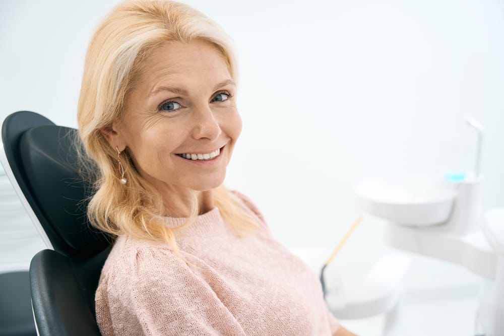 Smiling Woman After Dental Treatment – Bridges Dental Services in Irvine A middle-aged woman with a radiant smile sits comfortably in the dental chair, showing confidence and satisfaction after a successful restorative treatment – Bridges Dental Services in Irvine.