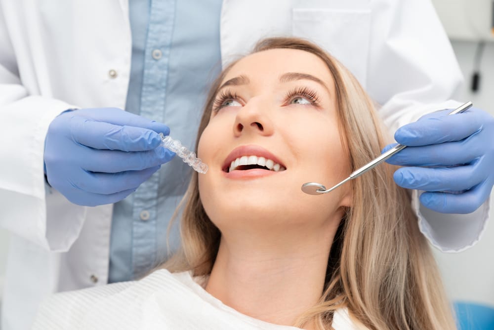 Patient Smiling During Invisalign Consultation – Restorative Dentistry Long Beach A woman in a dental chair smiles as her dentist presents a clear aligner, representing advanced orthodontic and restorative treatment options – Restorative Dentistry Long Beach.