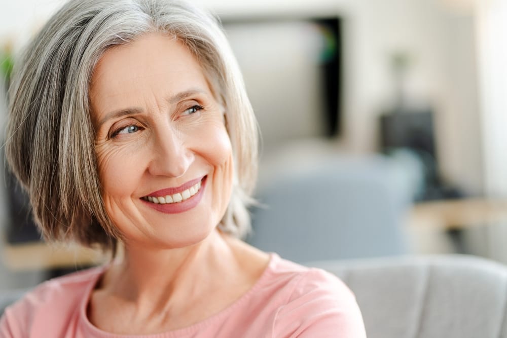 Confident Senior Woman Smiling – Long Beach Dentures A graceful older woman with short gray hair smiles warmly, showing comfort and confidence with her natural-looking dentures – Long Beach Dentures.
